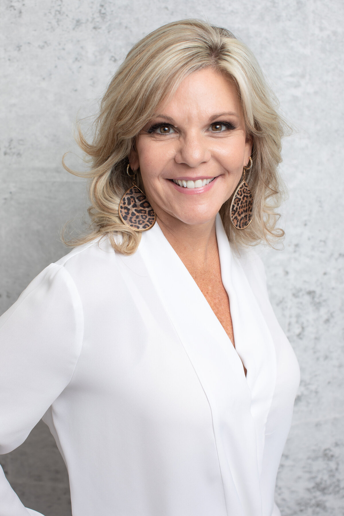 Cincinnati portrait capturing a radiant woman with wavy blonde hair, donning statement leopard-print earrings and a white blazer. The image highlights poised and sophisticated studio photography.