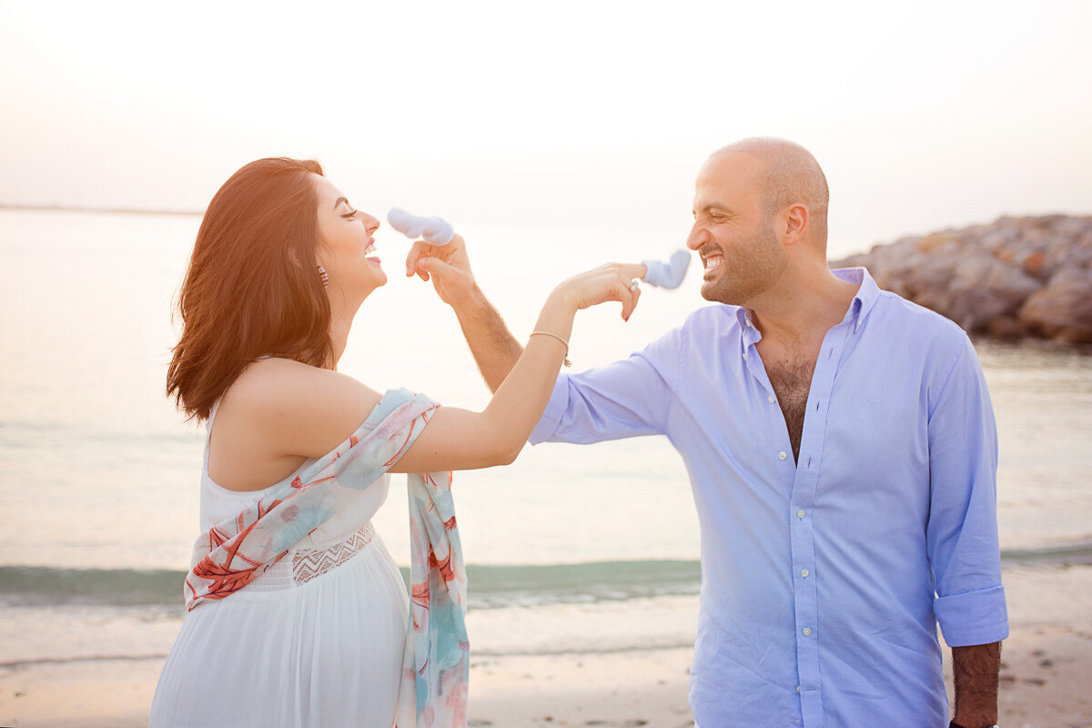 Couple playing blue baby socks in their pregnancy beach photo shot in Victoria British Columbia.