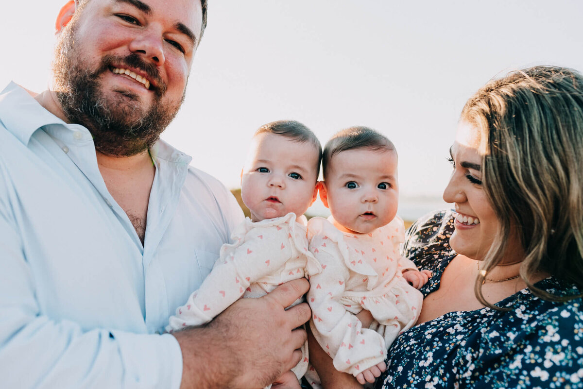 A mother and father hold their twin daughters while their daughters look at the camera at sunset