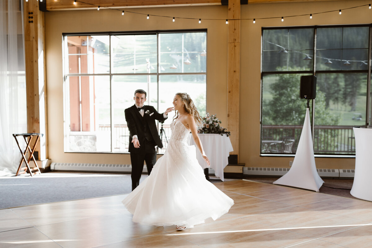 Bride and groom perform their first dance in a bright reception venue in Breckenridge, Colorado, with large windows showing lush green scenery in the background.