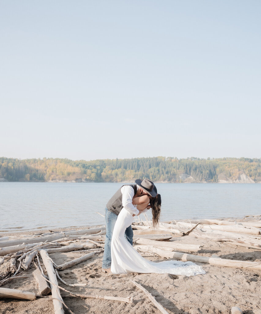 Couple kissing on driftwood covered beach, captured by Ninth Avenue Studios, elegant and romantic wedding photographer in Saskatoon, Calgary and Vancouver. Featured on the Bronte Bride Vendor Guide.