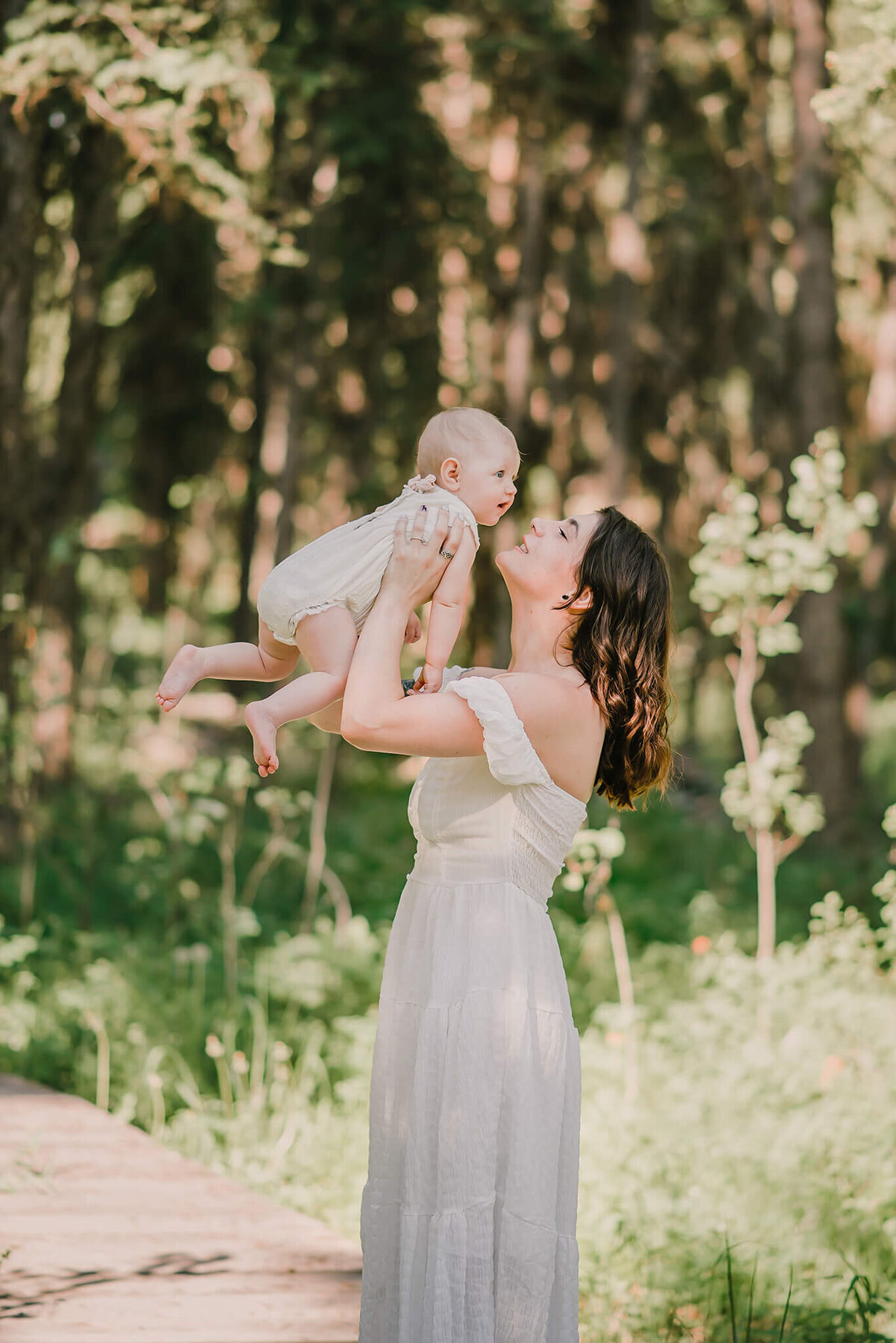 Brittany Danielle captures a loving portrait of a mother and daughter in matching white dresses. Mother hold her daughter up in the air and the smile at eachother.