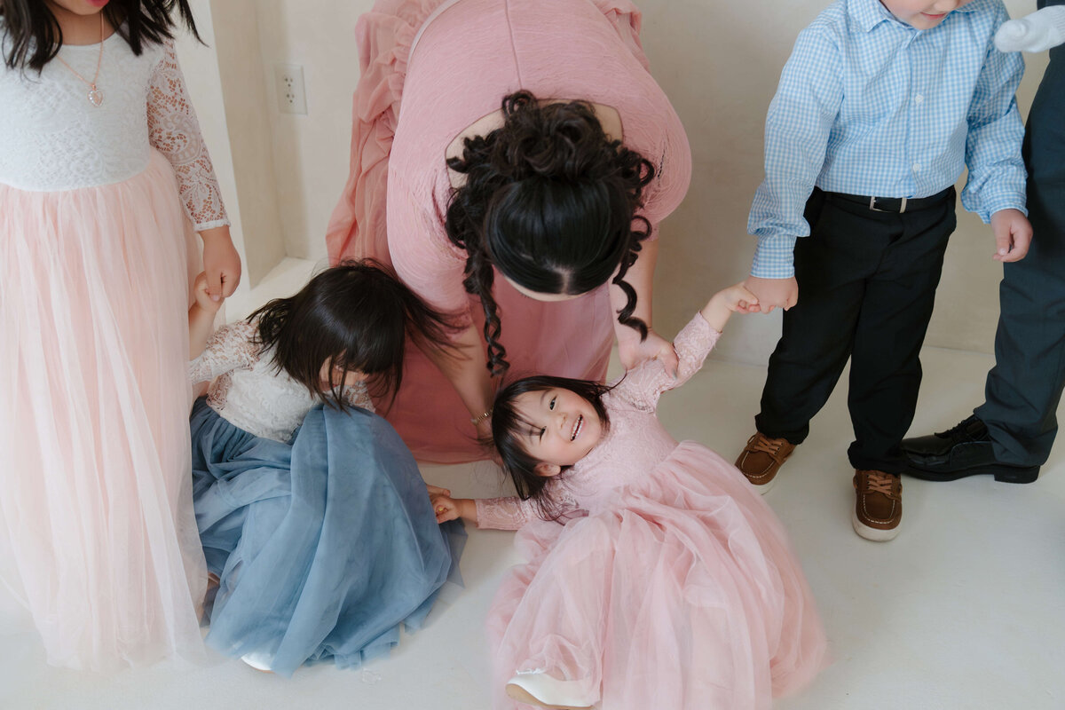 Mother helping her children up with laughter as one lies on the floor during a playful family session.