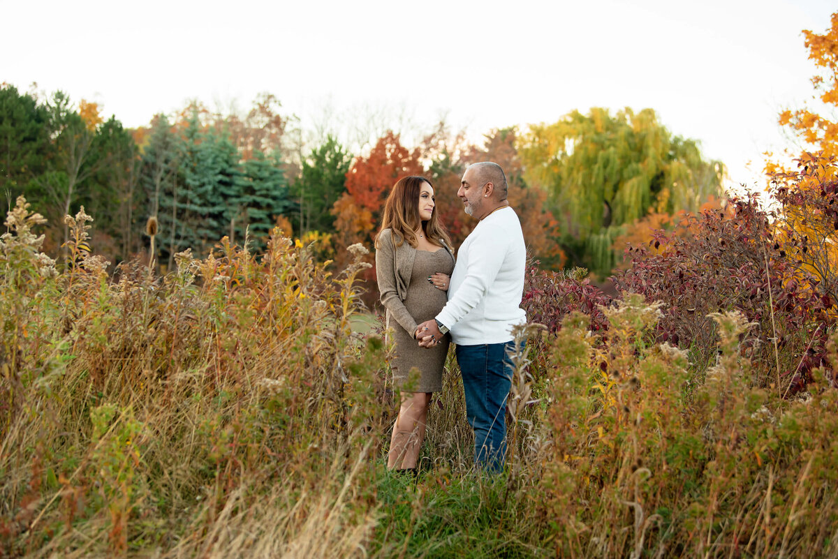 husband and wife standing in a field for their fall maternity photos in Burlington, ON