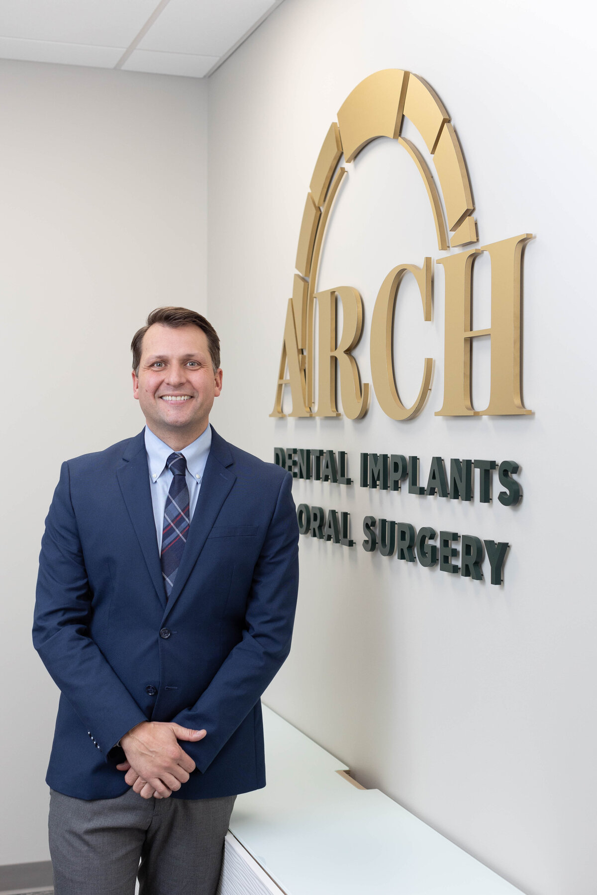 Smiling dentist standing in front of his logo