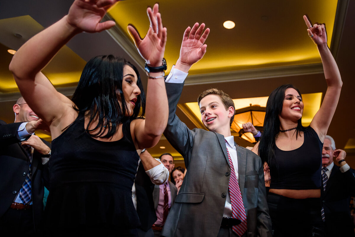 A boy in a suit dances with two women on the dancefloor