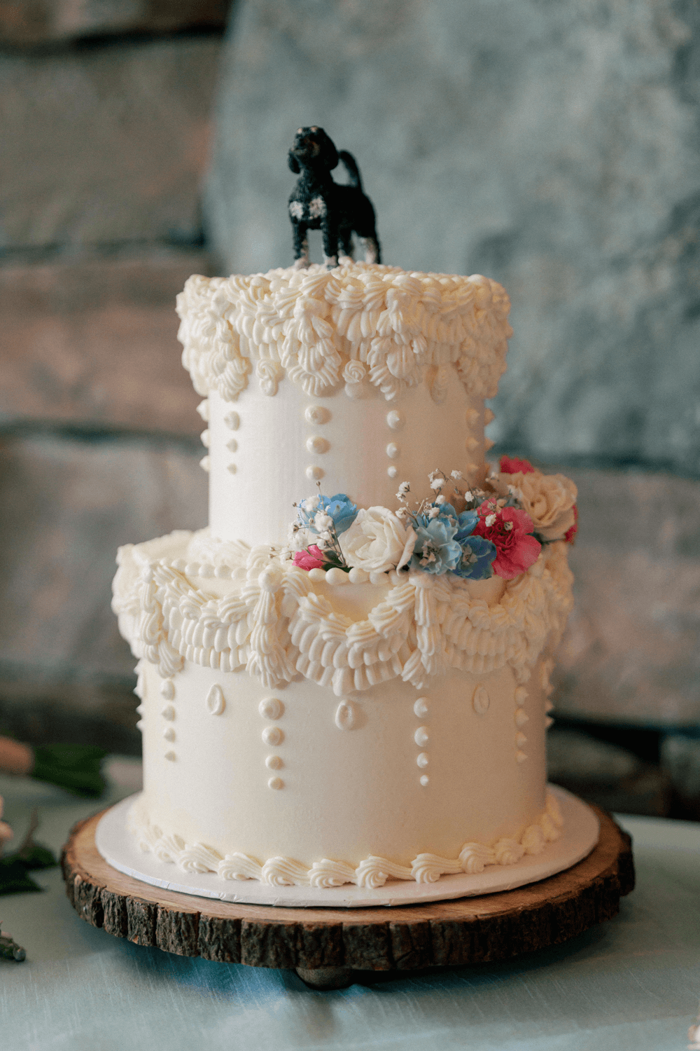 two-tier wedding cake with vintage piping, pastel florals, and a black dog cake topper at a summer wedding in Moonlight Basin.