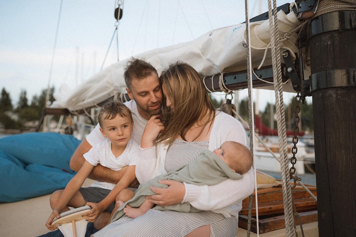 family of four on sailboat with swaddled newborn baby boy