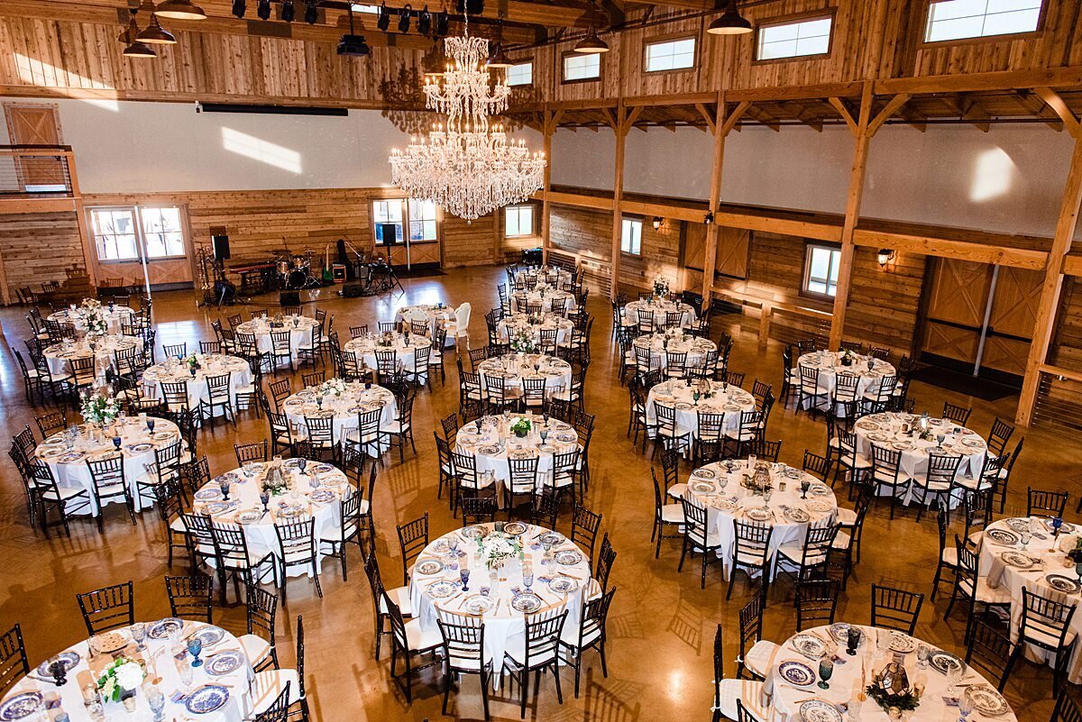 Many round tables set with white table cloths and brown chiavari chairs for a luxury barn wedding reception at Sycamore Farms