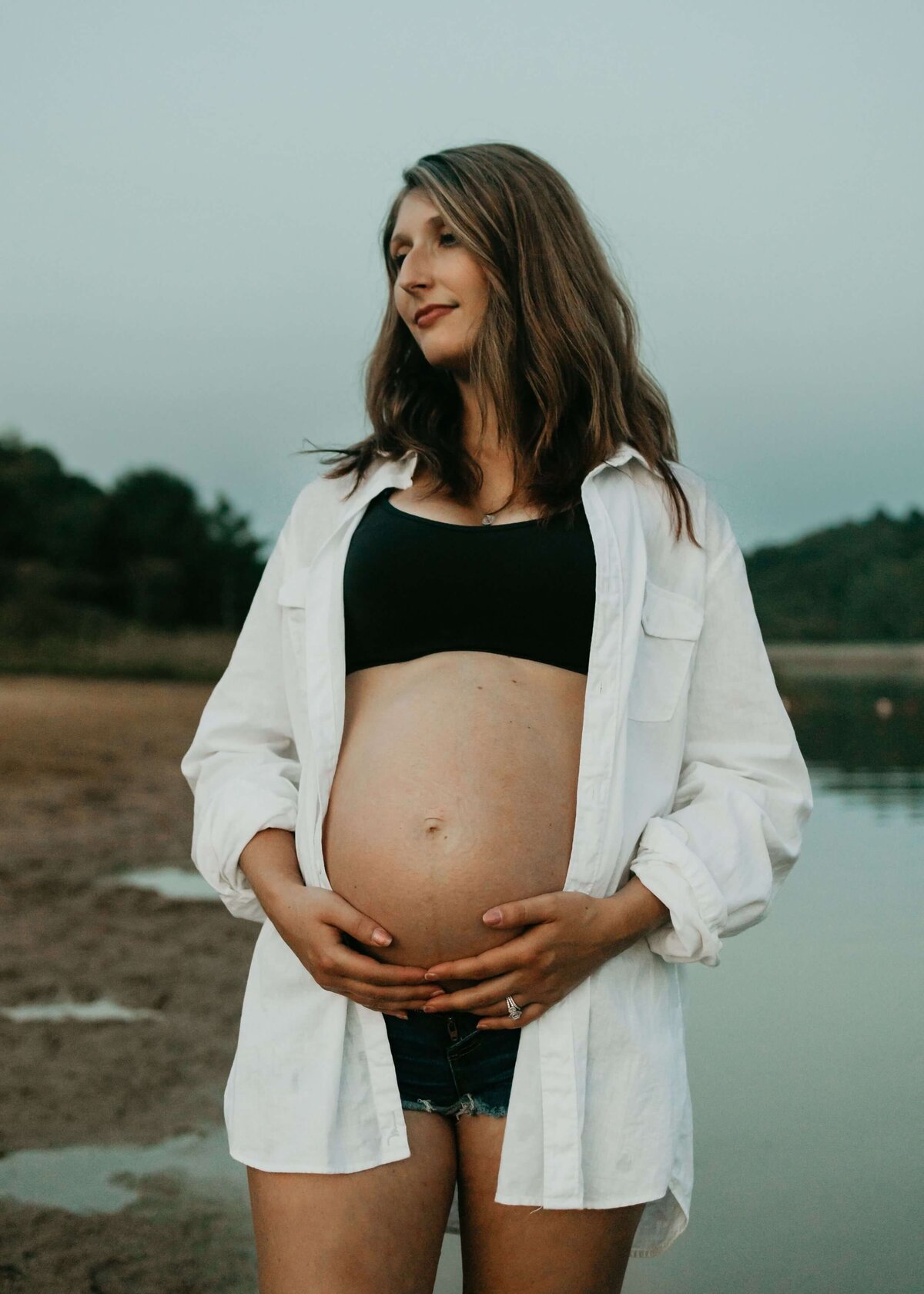 A pregnant woman standing by a body of water captured beautifully by a Pittsburgh maternity photographer.