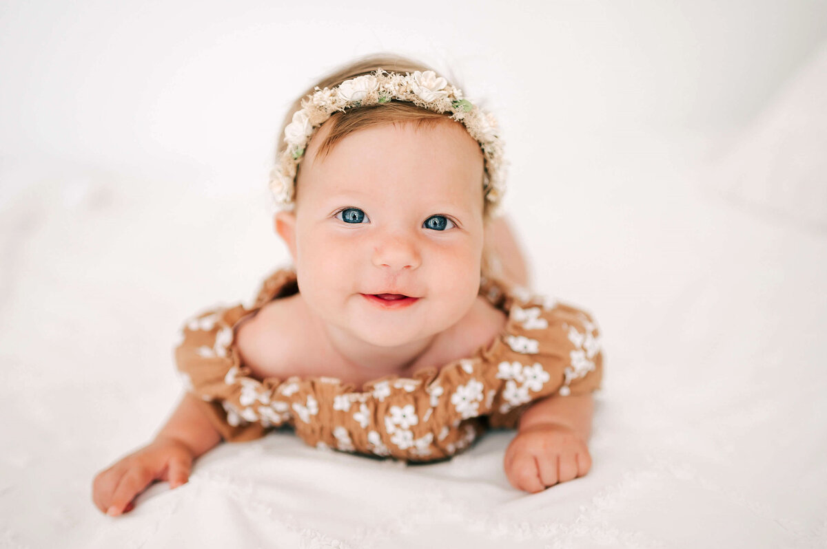 milestone baby portrait in Branson MO of little girl in floral dress smiling on bed