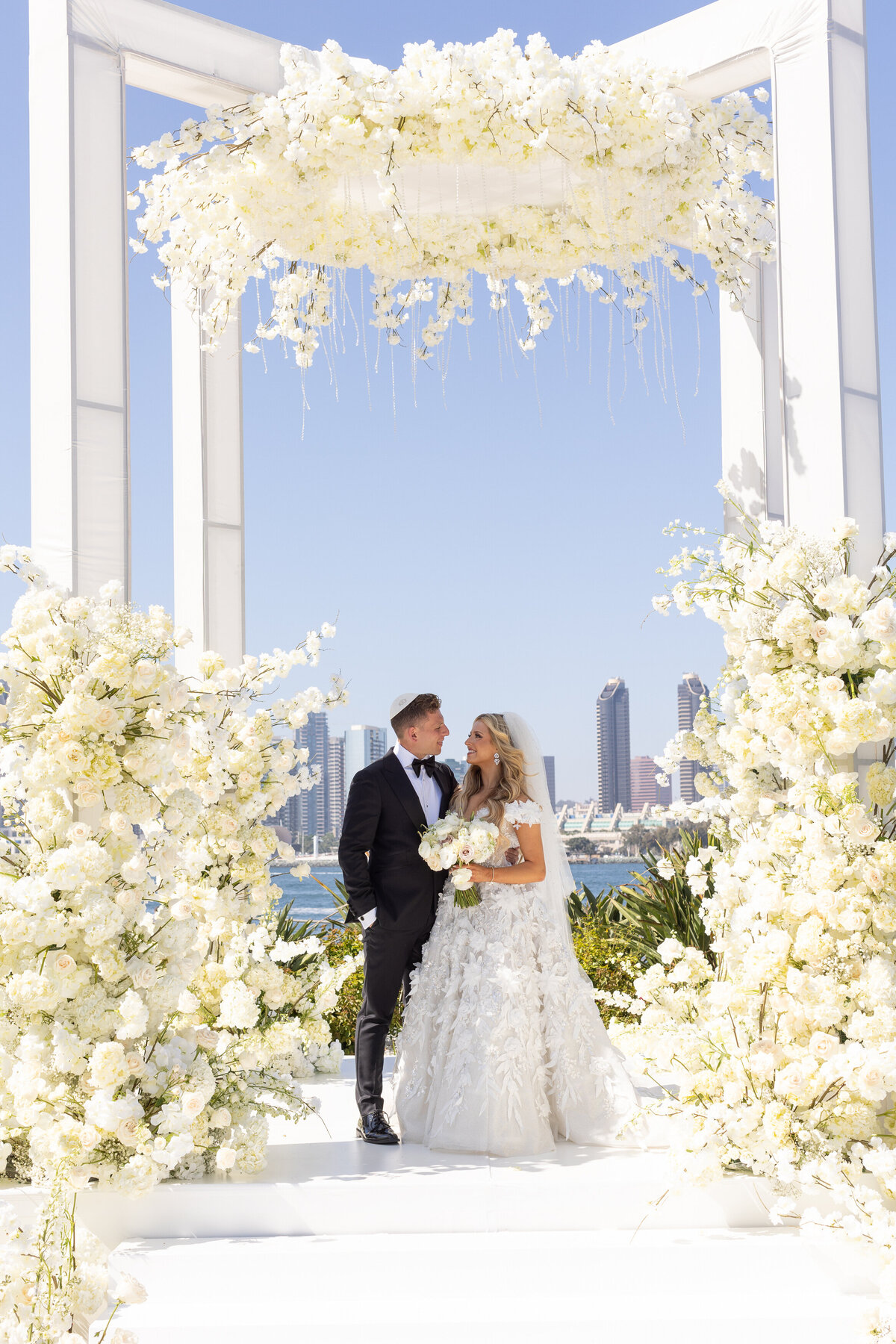 A groom with his arms around a bride as they smile at each other