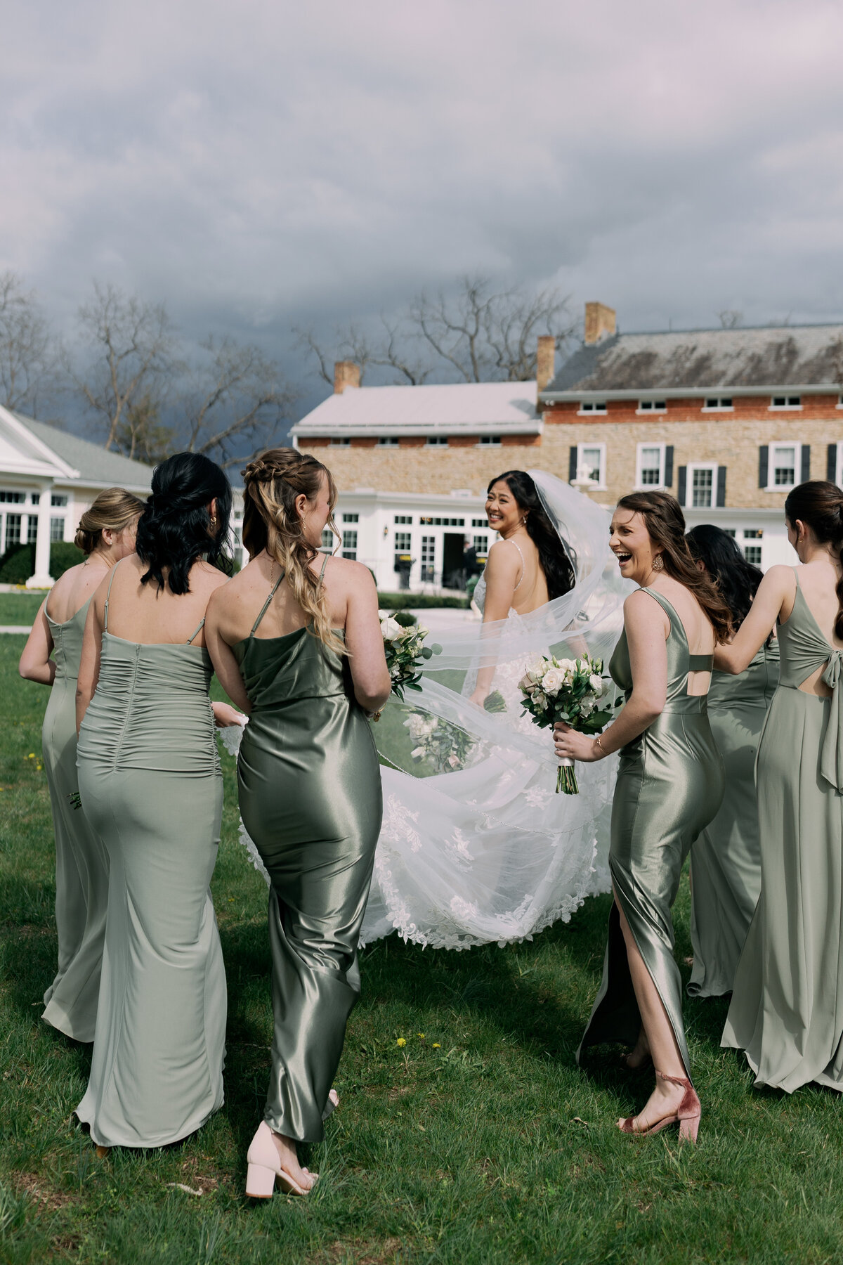 Bridesmaids in sage green satin gowns holding white rose bouquets at Springfield Manor wedding.