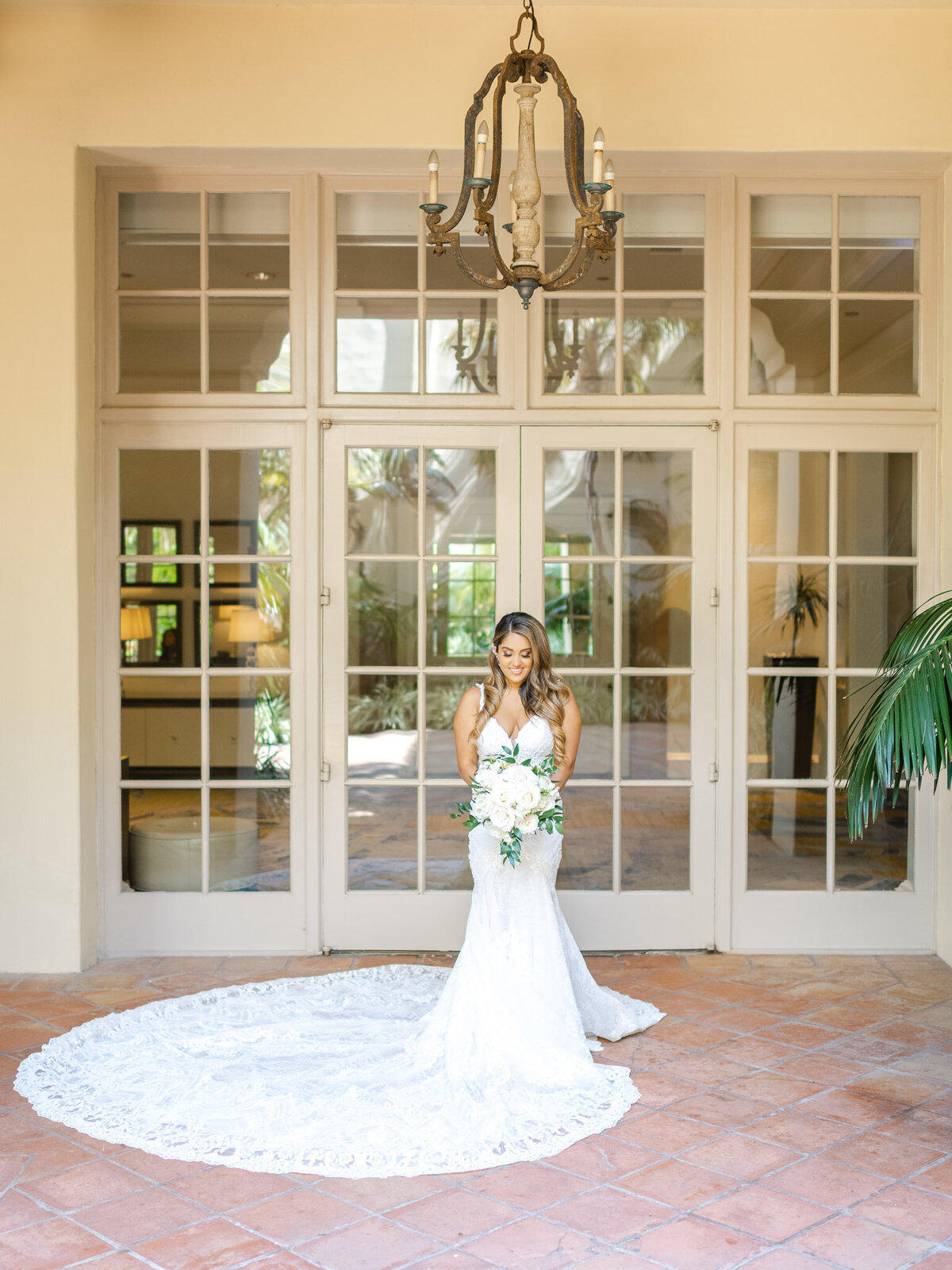 The bride poses with her bouquet in front of elegant French doors at the Ritz-Carlton Laguna Niguel, her lace train beautifully spread behind her