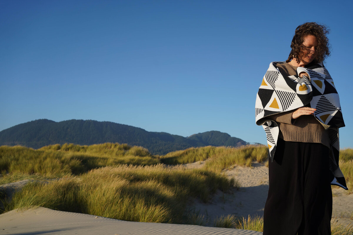 Woman standing on a windy beach with her shoulders wrapped in a blanket