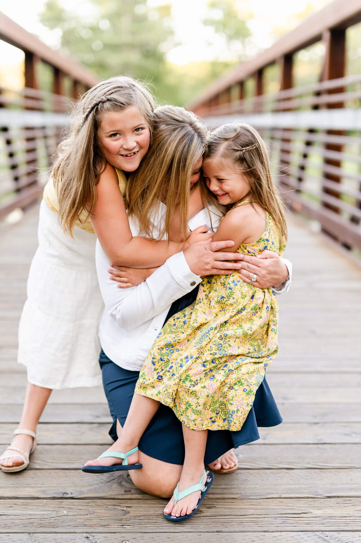 Daughters hugging mom  and laughing  while on a bridge near Geneva, iL.