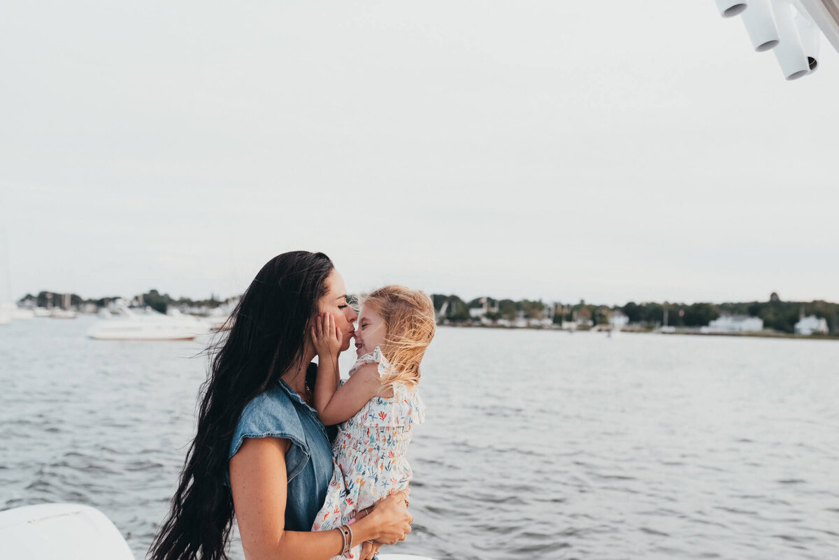 A mother gives her young daughter a kiss on the nose on their family boat at sunset