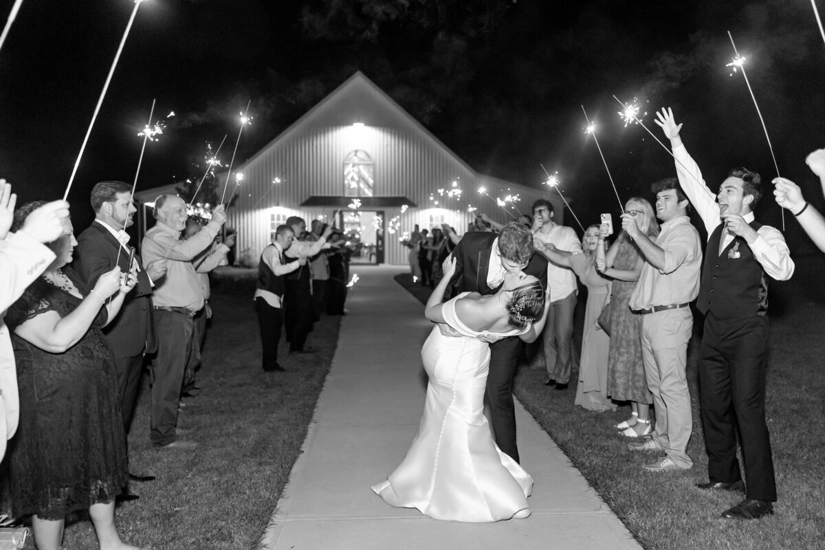 Groom dipping his bride as he kisses her and guests cheer
