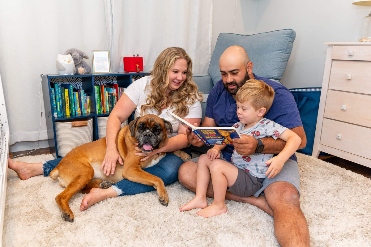 Lifestyle family session for a sweet family at their home, reading a book to their toddler while all cuddled together, including their dog.