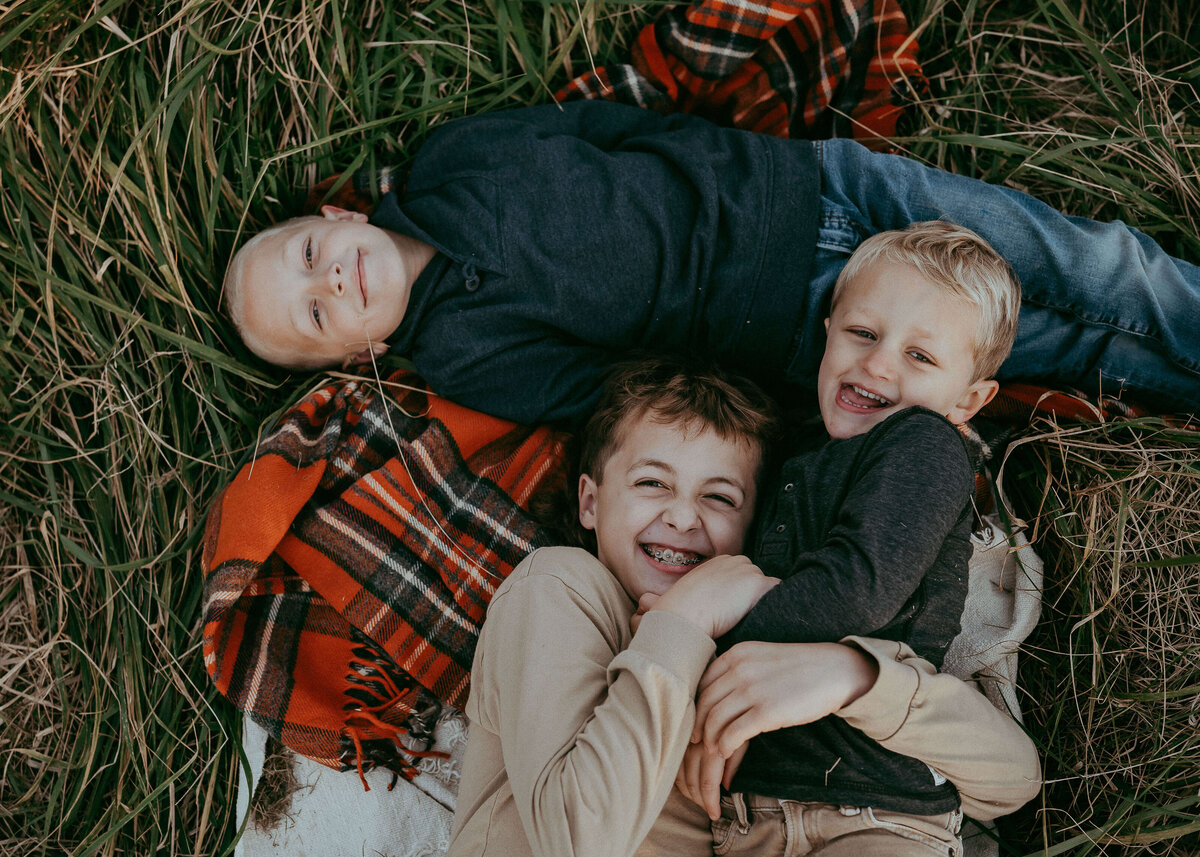 A vibrant colored portrait of three brothers tickling each other while laying on a plaid blanket during their family photo session.