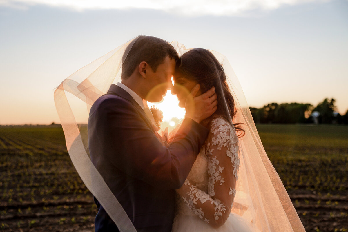Wedding couple share an intimate moment in the sunset under her veil.