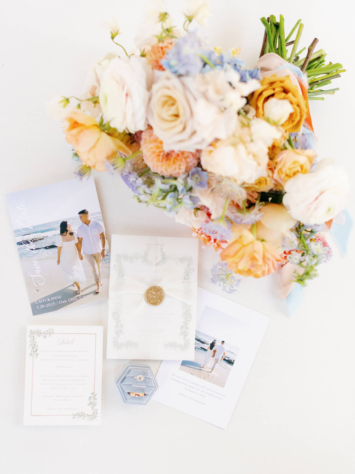 A romantic flat lay features a bouquet of pastel flowers, wedding invitations, and a blue ring box with two rings. The tone is elegant and joyful.