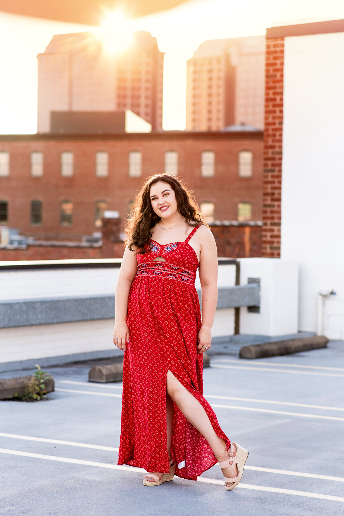 RVA senior girl wearing long red dress poses at sunset on a rooftop downtown RVA.