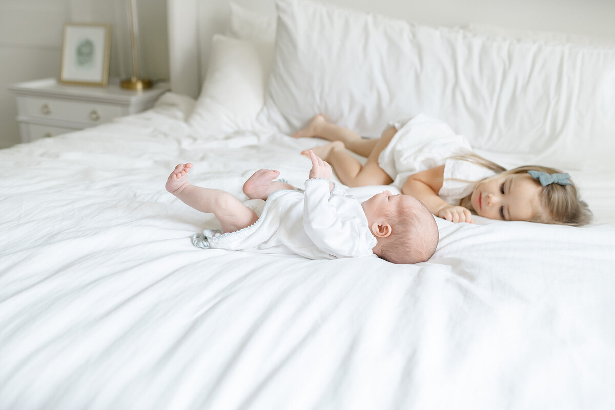 a toddler hanging out with her sibling on a white bed