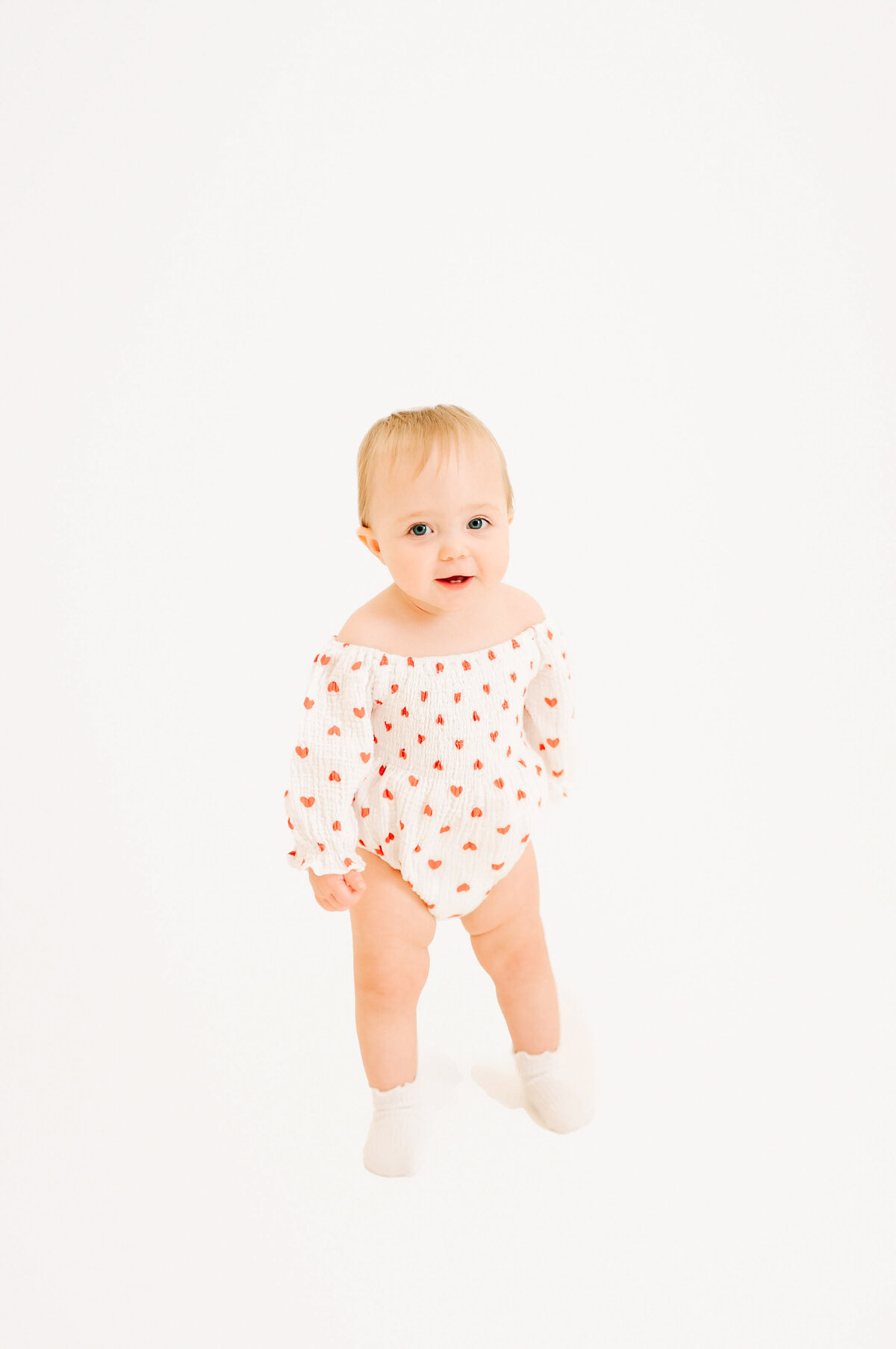 toddler girl in heart outfit smiling during her 1st birthday milestone photography session in Springfield MO