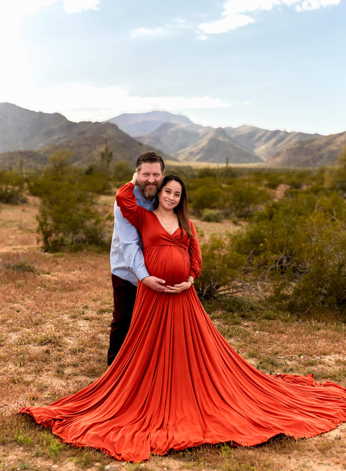 Expecting mother reaching up to hold her husband close while they cradle her growing belly. Photographed by Cactus & Pine Photography