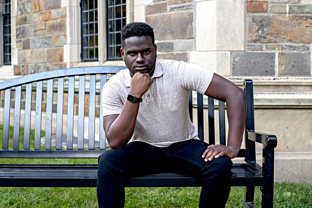 African American male wearing tan polo shirt and black jeans sitting on a bench