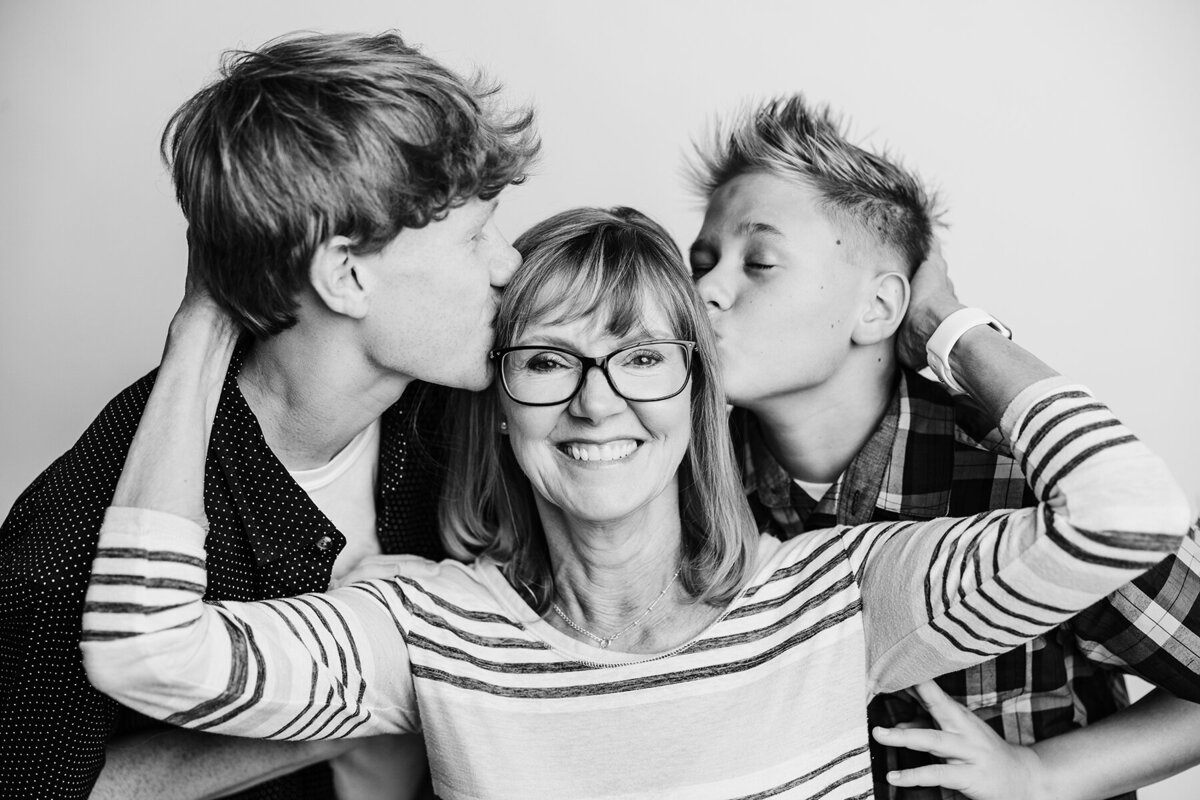 Black and white photo of grandma with her grandsons kissing her