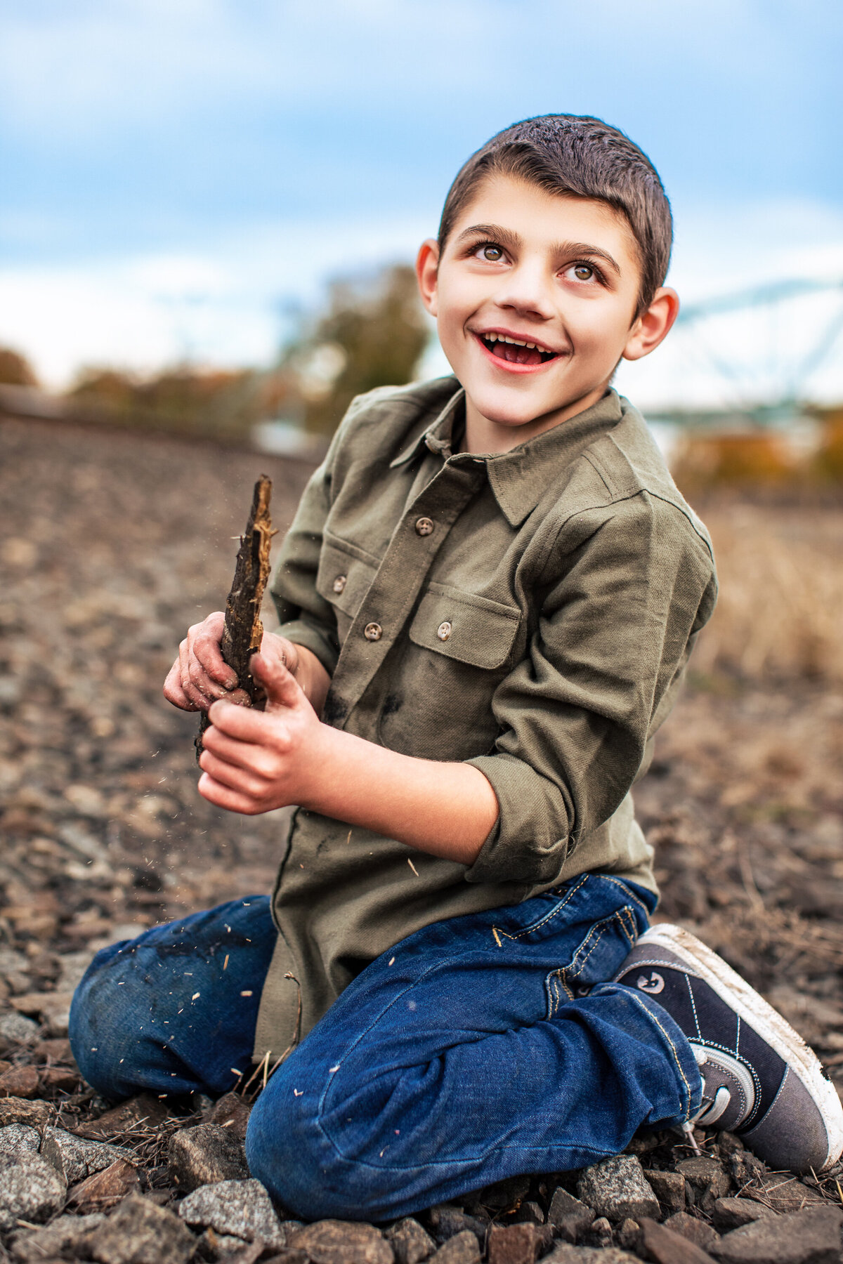 A young boy plays with a stick in the woods near the Sewickley bridge during a children's photography session
