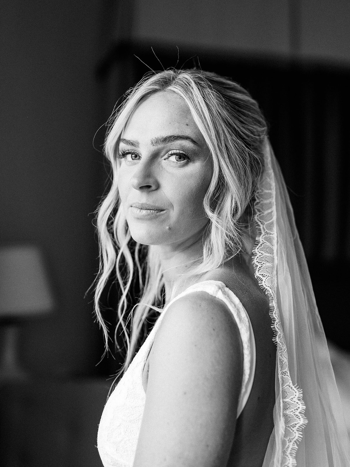 A black and white portrait of a bride as her hair falls to the side of her face and her veil falls behind her