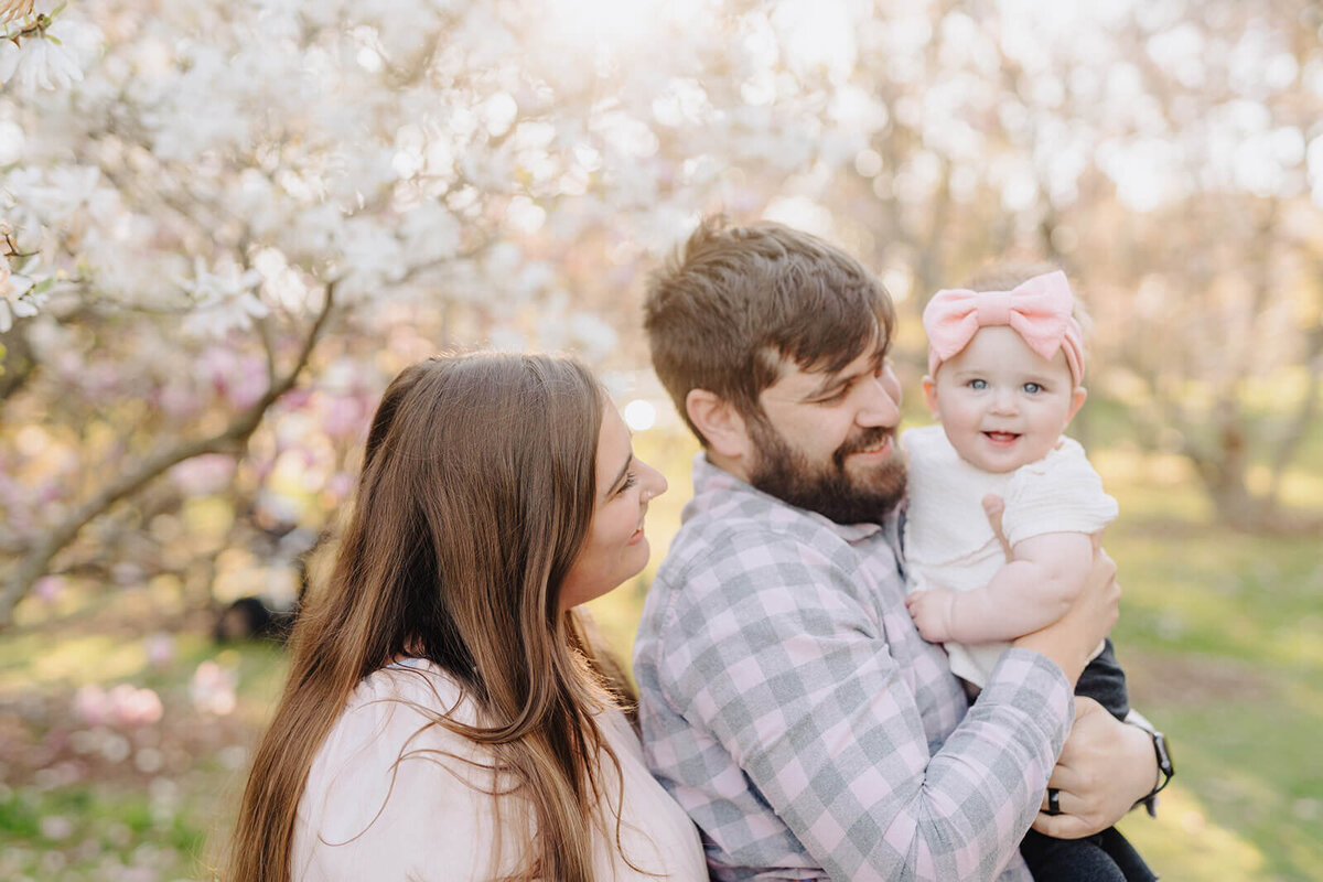 couple looking at baby standing in front of a cherry blossom tree in Finger Lakes, NY