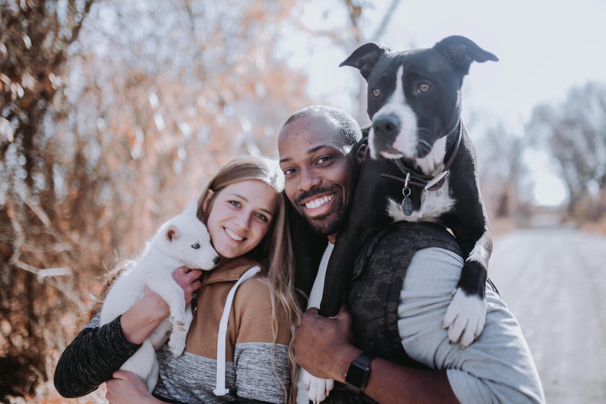 man and woman standing together while holding their two dogs for their fall family photos documented by Idaho Falls family photographer