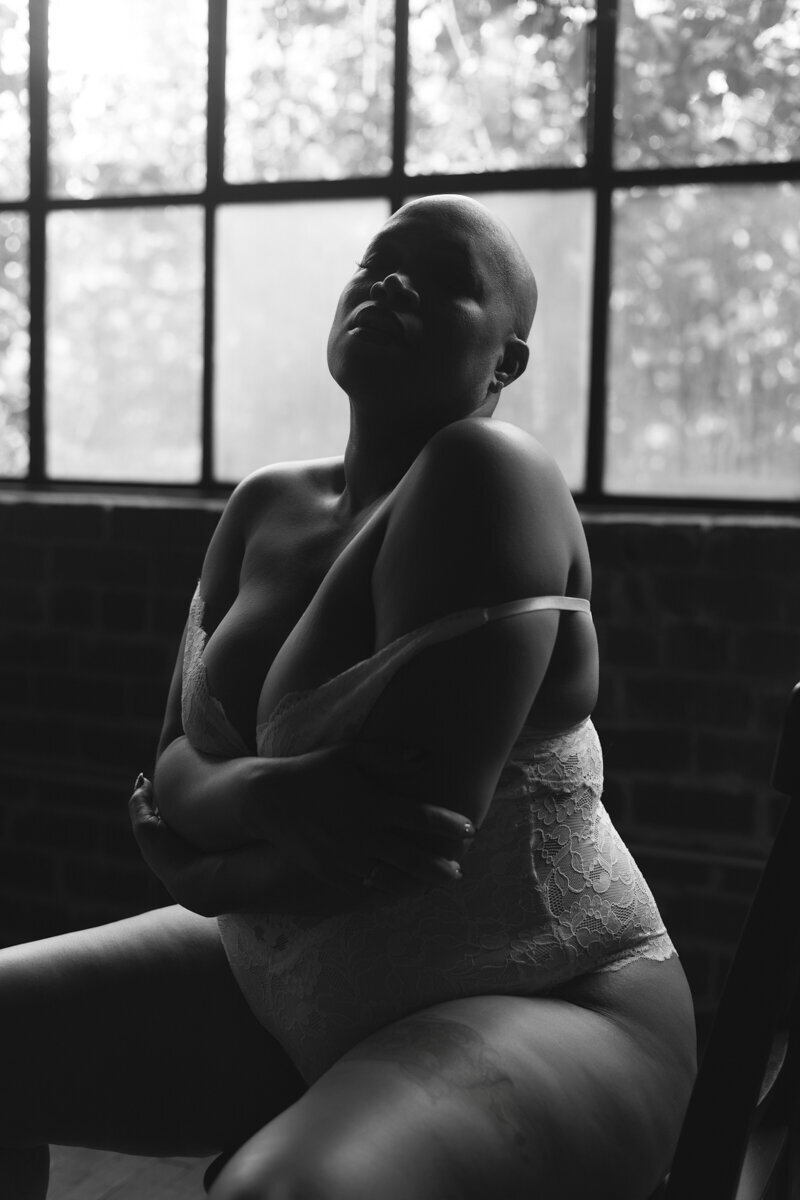 artistic black and white boudoir photo of a bald woman sitting on a chair, embracing herself