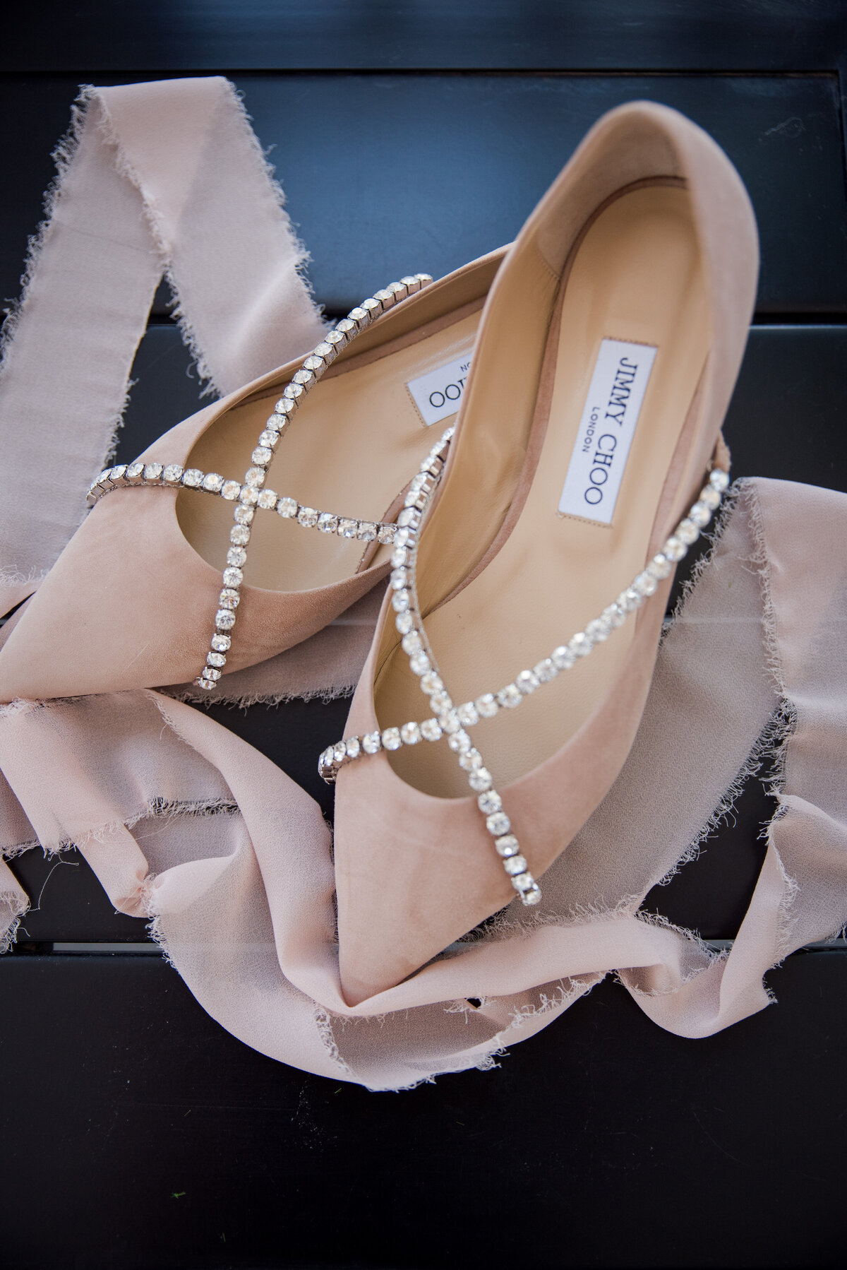 A pair of bridal Jimmy Choo shoes that are light pink with rhinestones.