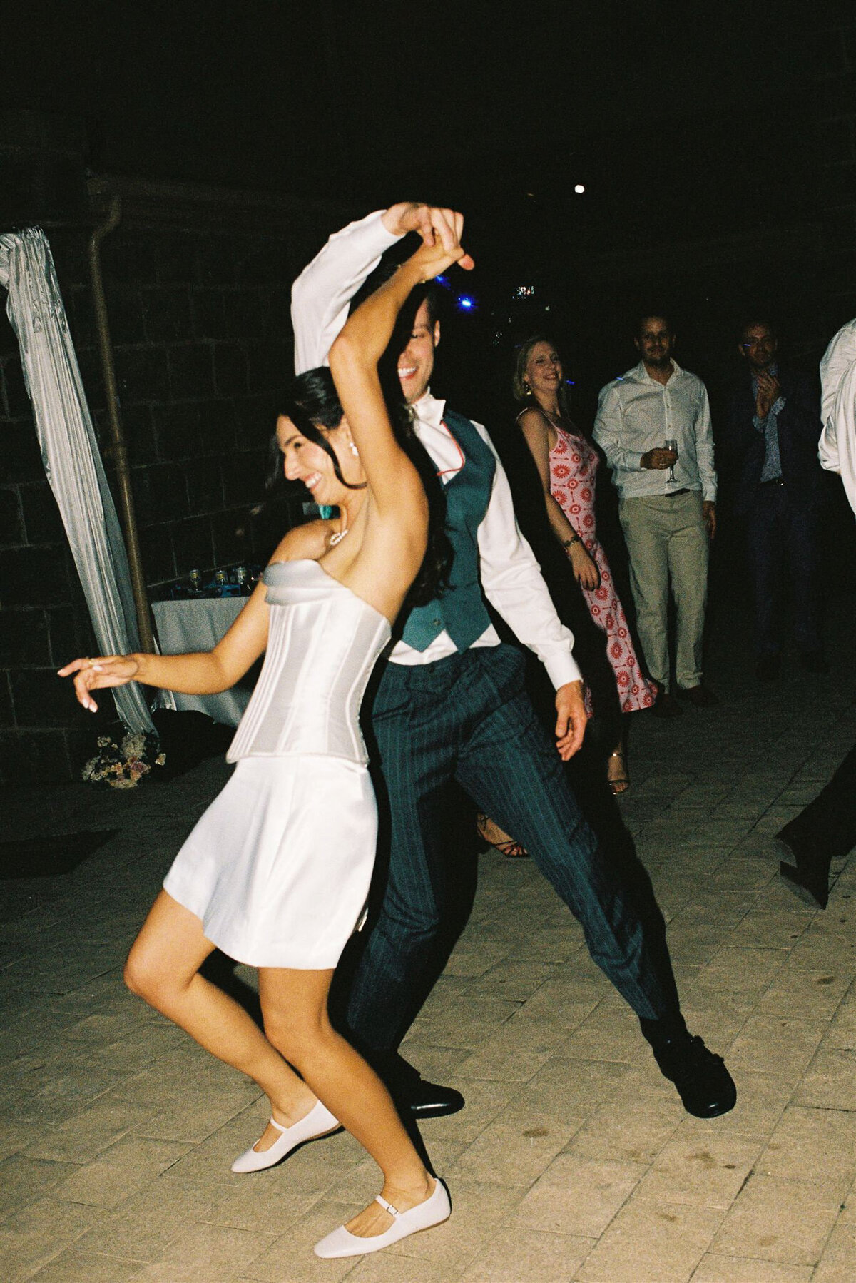 Couple laughing and dancing together on the floor during their micro-wedding celebration, captured naturally on 35mm film.