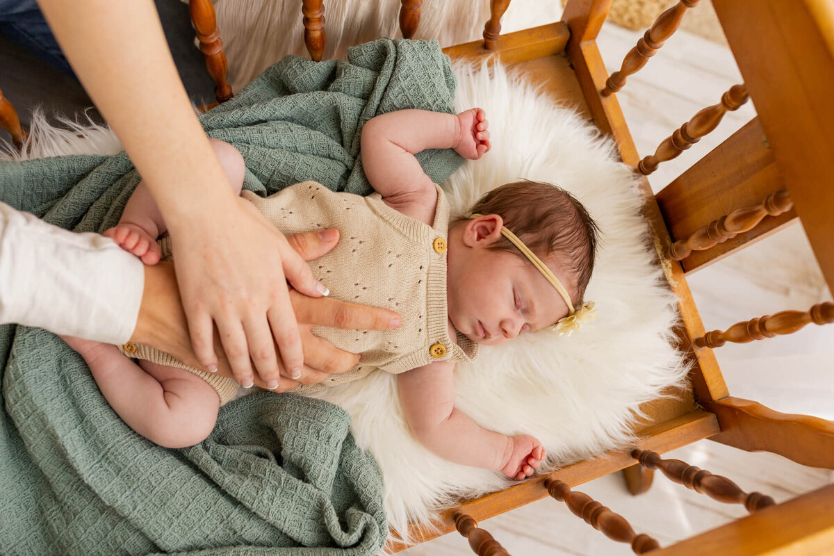 Mom and dad's hands on their newborn baby girl in a wooden bassinet