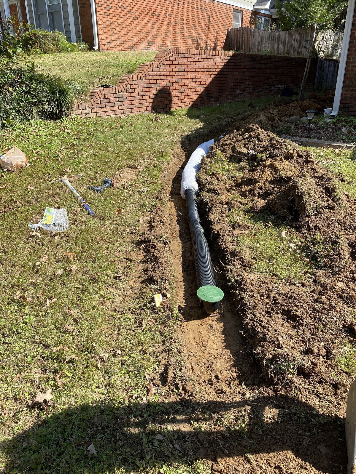 pipe-in-dirt-trench-in-front-yard-next-to-brick-wall