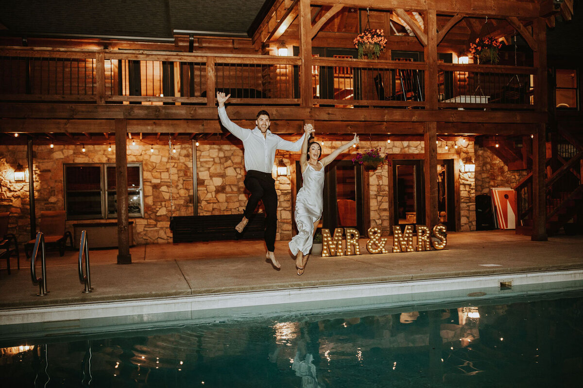 Newlyweds jumping into a pool with “Mr & Mrs” lights in the background