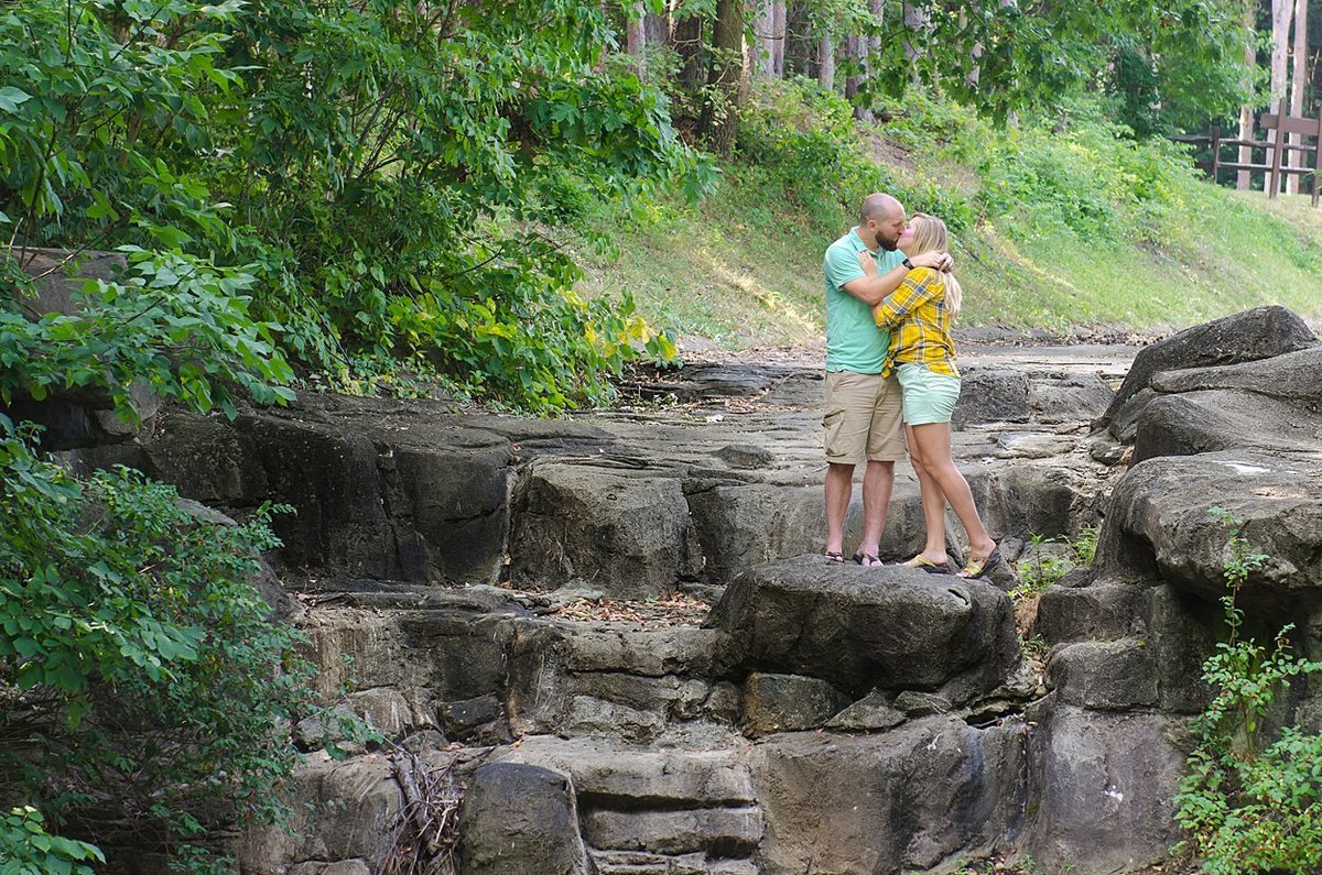 An engaged couple kisses on a dry waterfall during their engagement session at Twin Lakes Park in Greensburg, PA