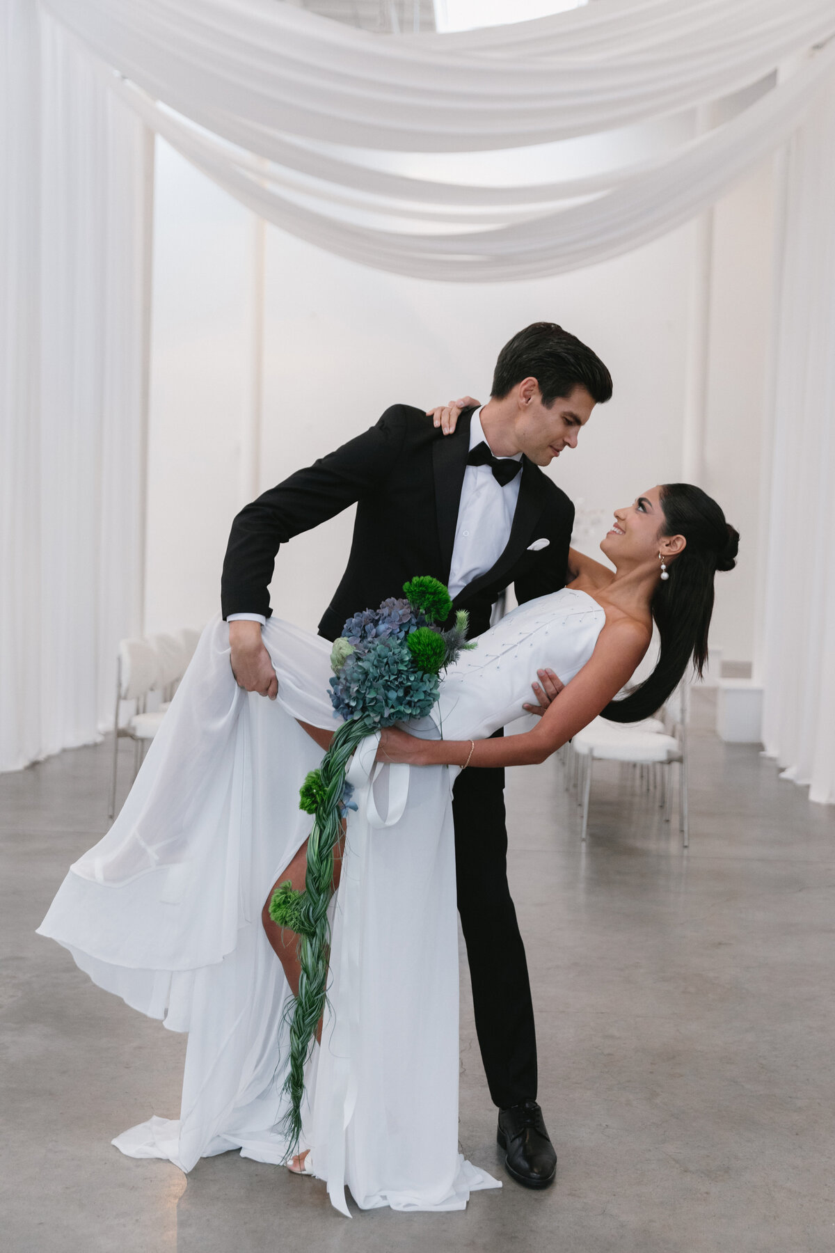 Bride and groom posing with a long cascading bouquet in a minimalist white New York City wedding studio.