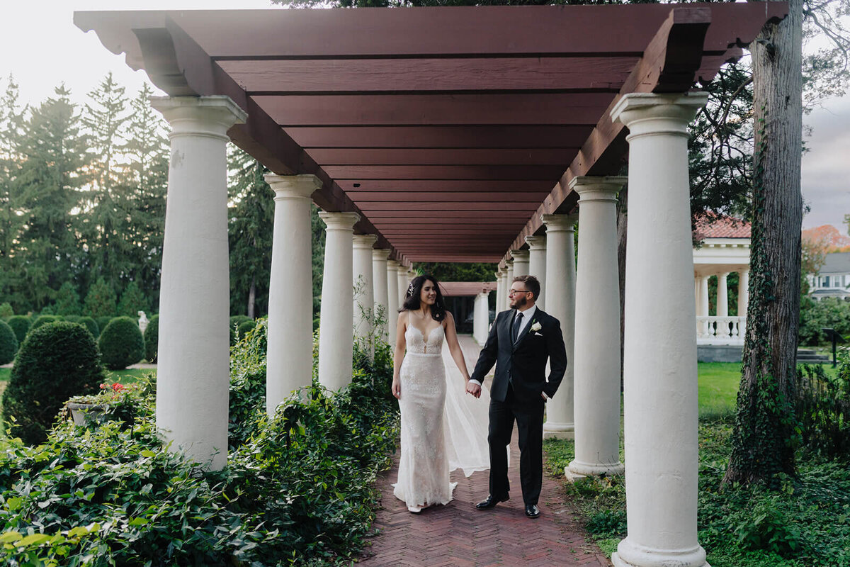 Bride and groom walking along by large white pillars at Finger Lakes wedding, NY