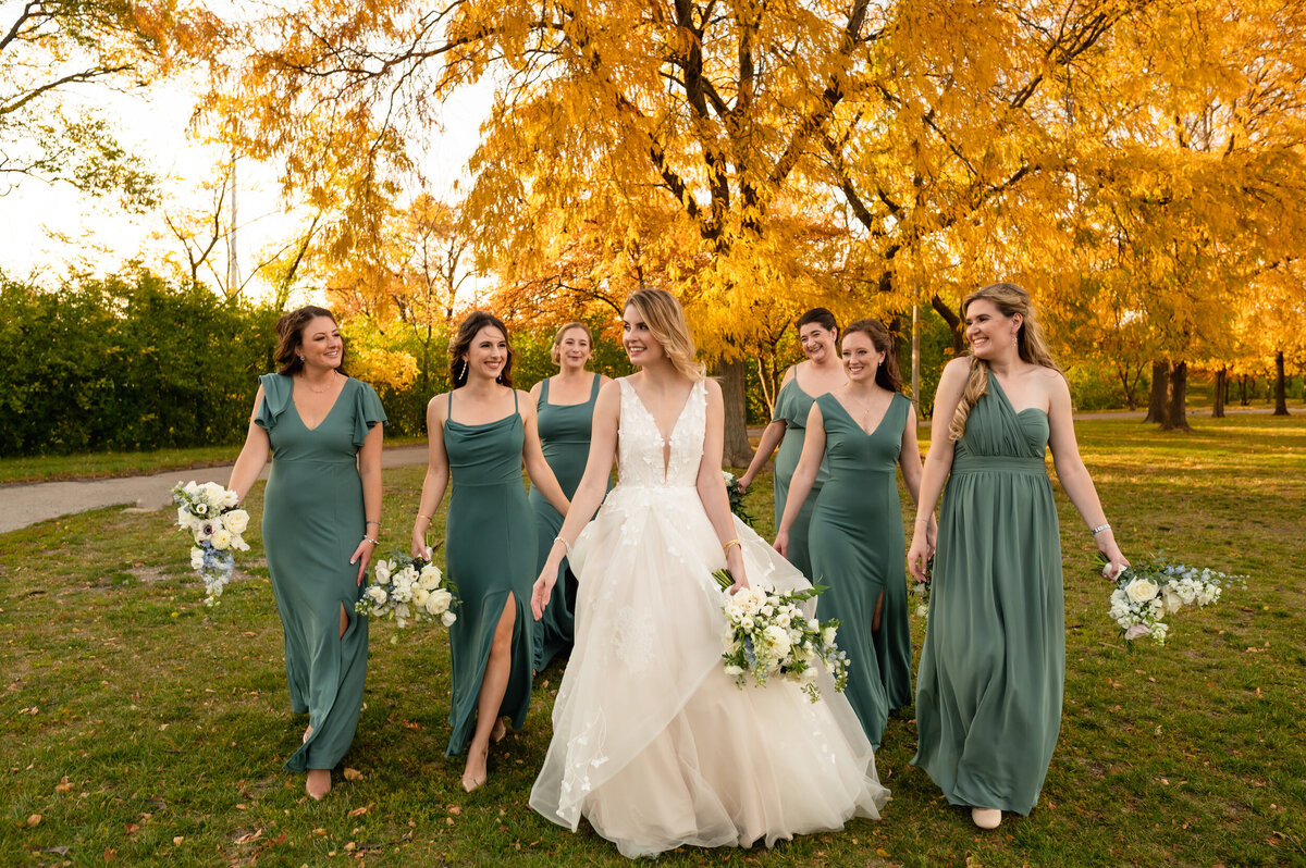 A bride walks with her bridesmaids  with fall colors surrounding them