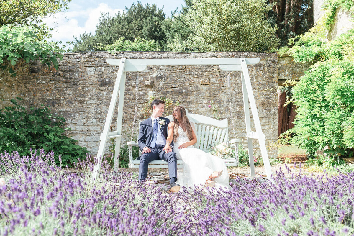 Bride and groom sitting on a swing seat in the lavender gardens at Caswell House
