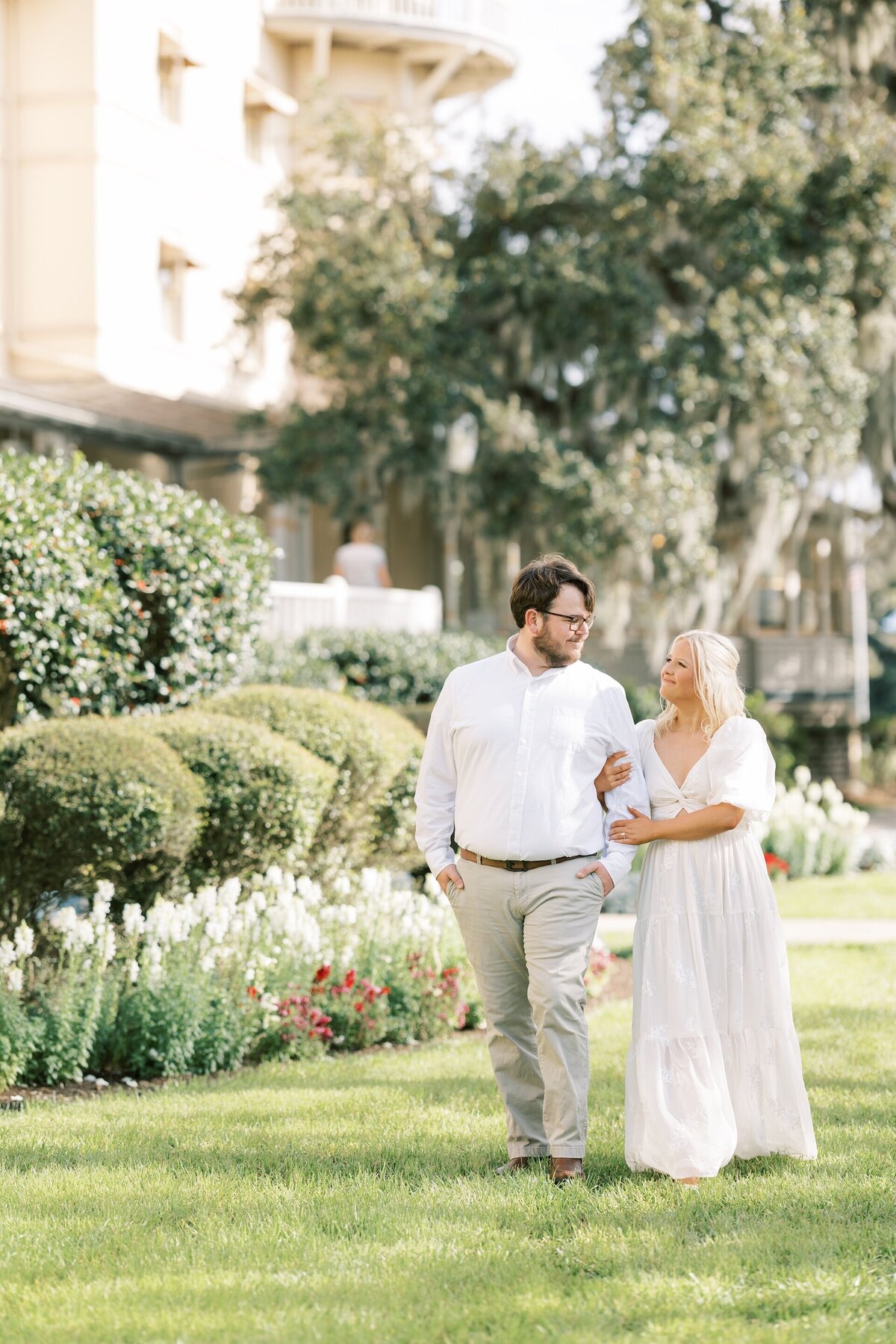 an engaged couple walking past a flower bed in a neighborhood