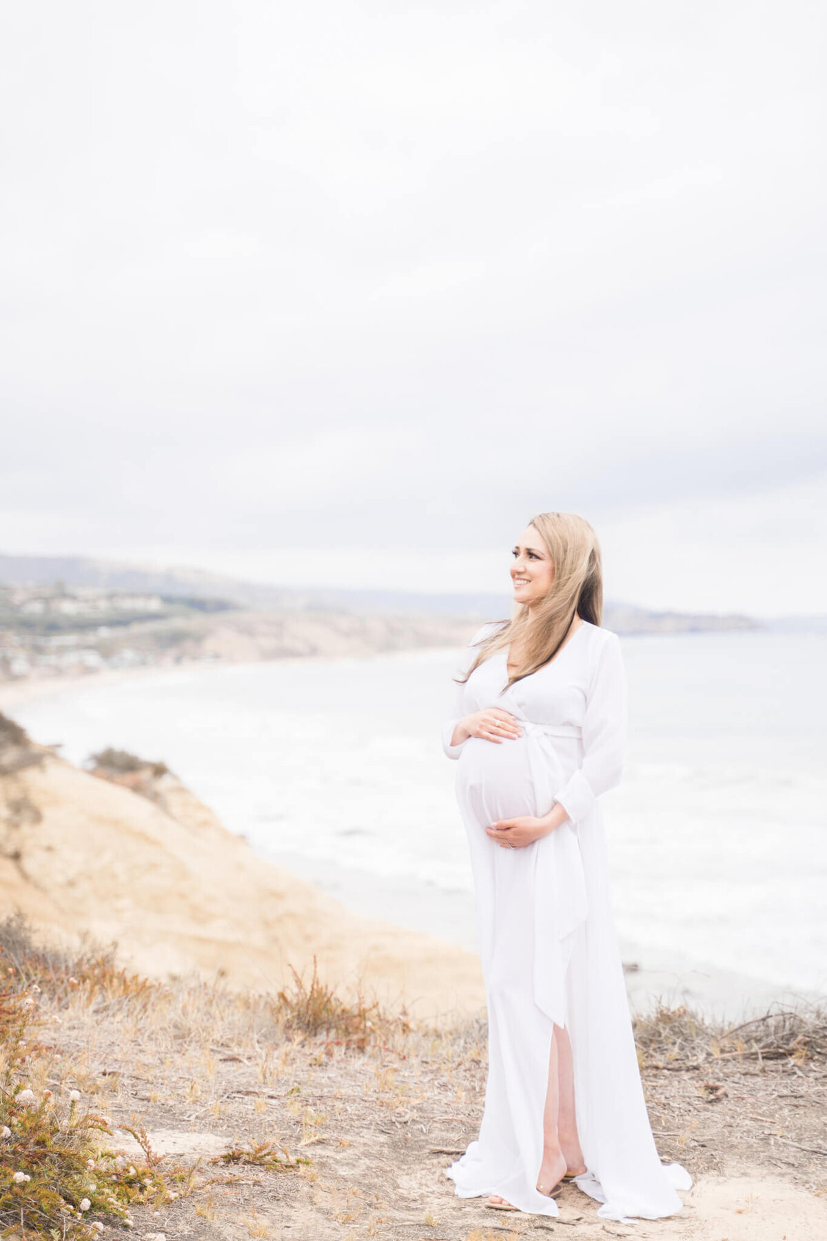 Pregnant mom in white dress on side of cliff in Southern California