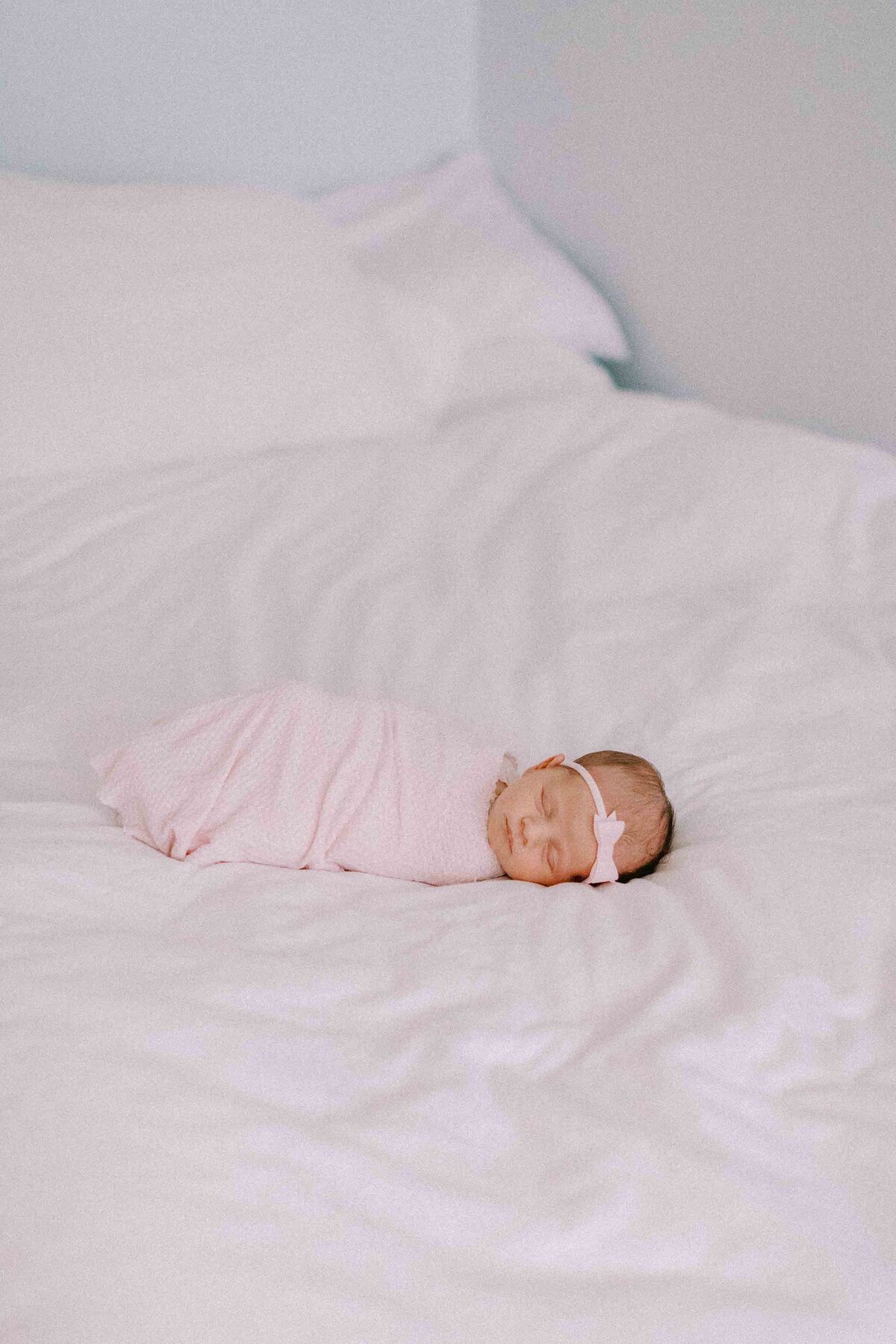 newborn baby girl wrapped in a pink swaddle and laying on a clean white bed